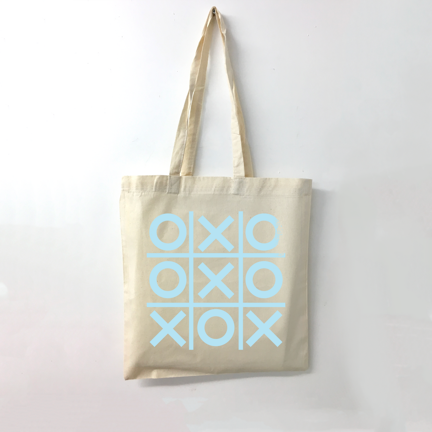 Beige tote bag with light blue 'XOXO' tic-tac-toe pattern on a white background