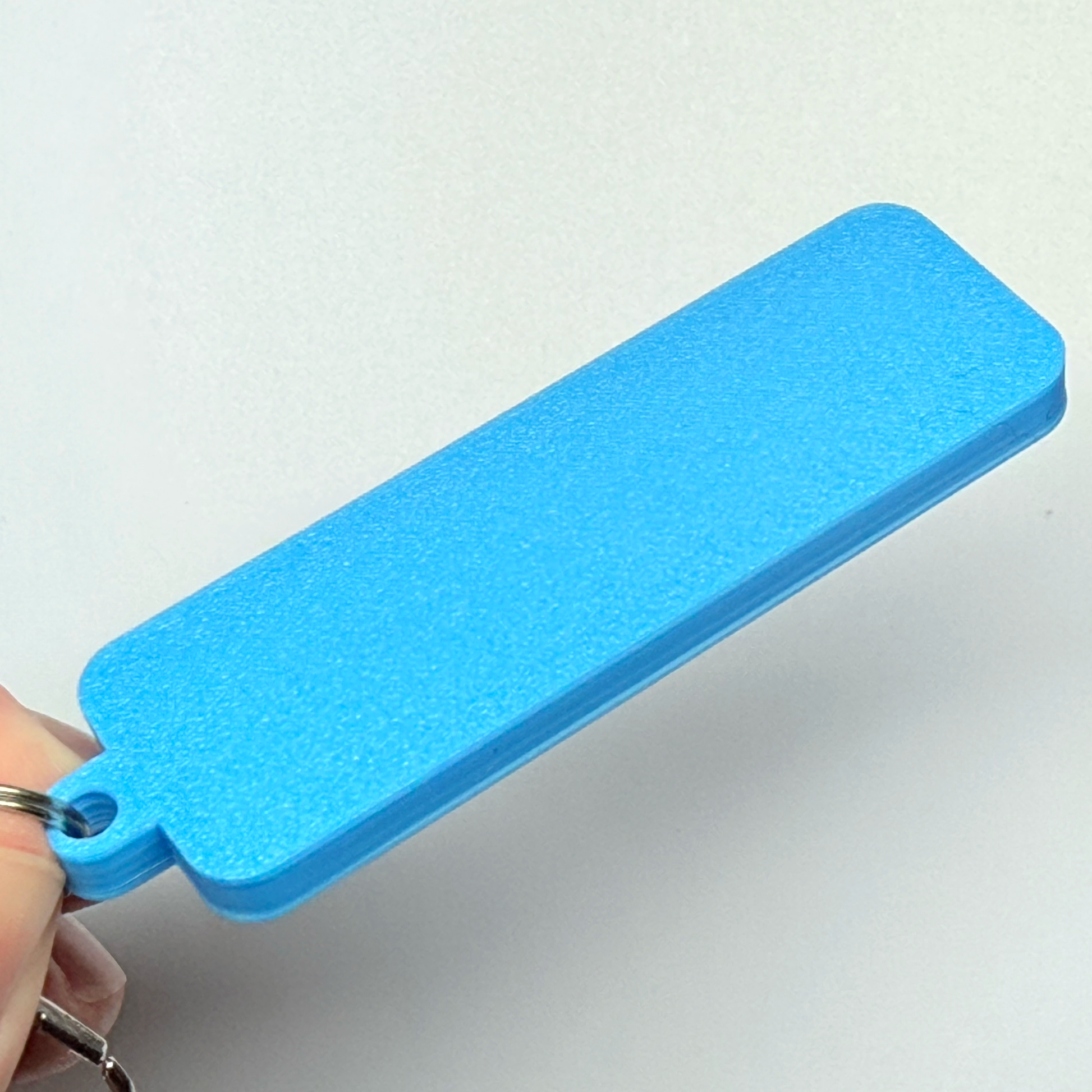 Blue rectangular plastic keychain held by a hand on a white background