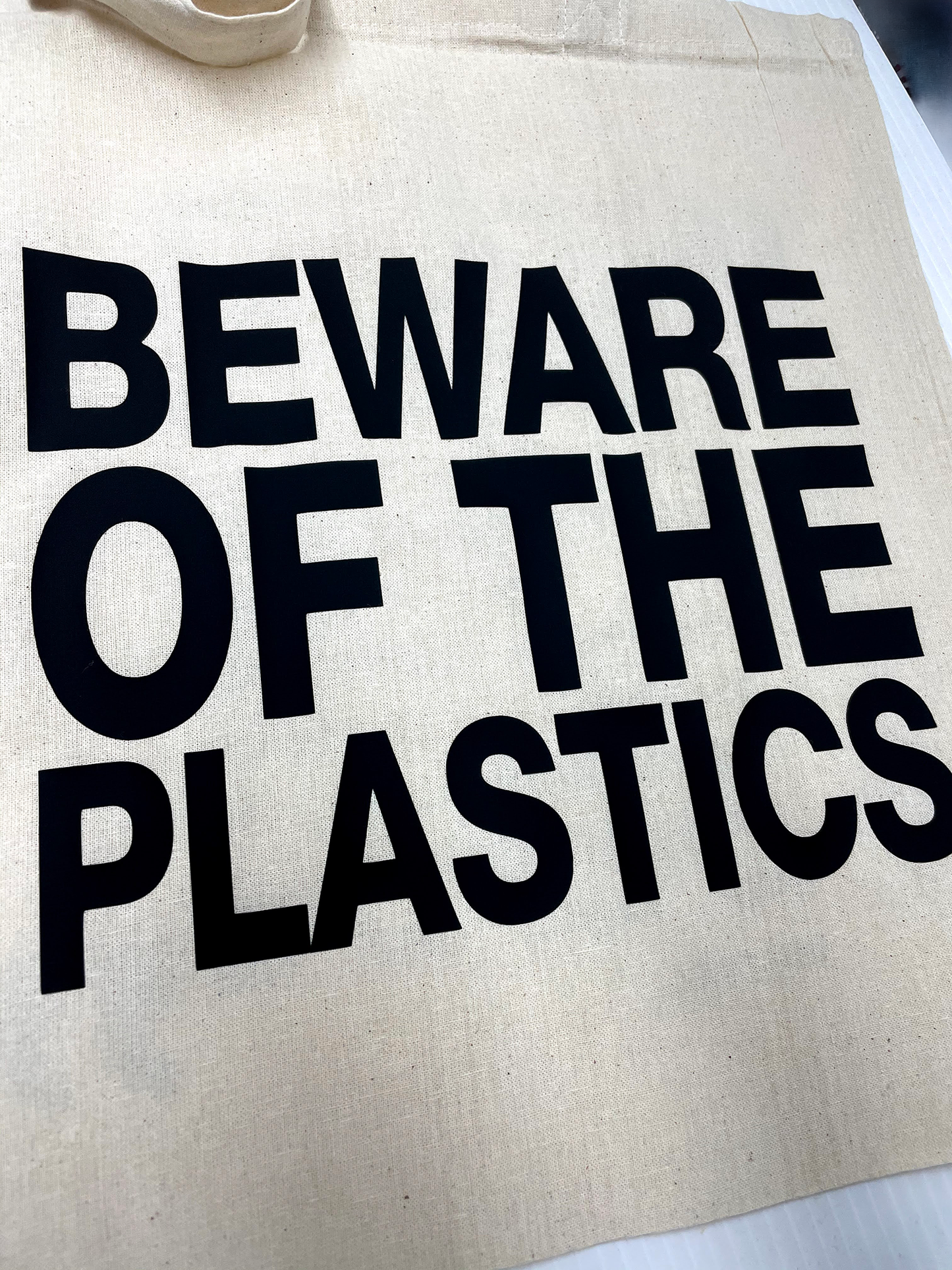 Beige tote bag with 'Beware of the Plastics' text in black.